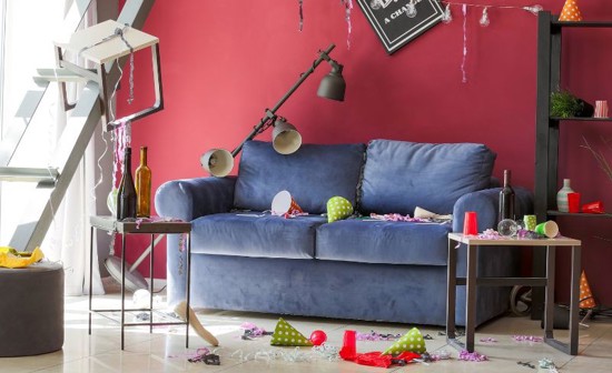 A sofa in a room with party cups and hats spread everywhere.