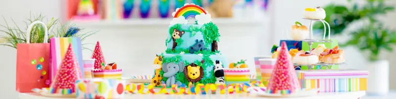 A cake with animals on surrounded by party food and favours.